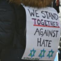 Person in a crowd wearing a placard that says "We stand together against hate"